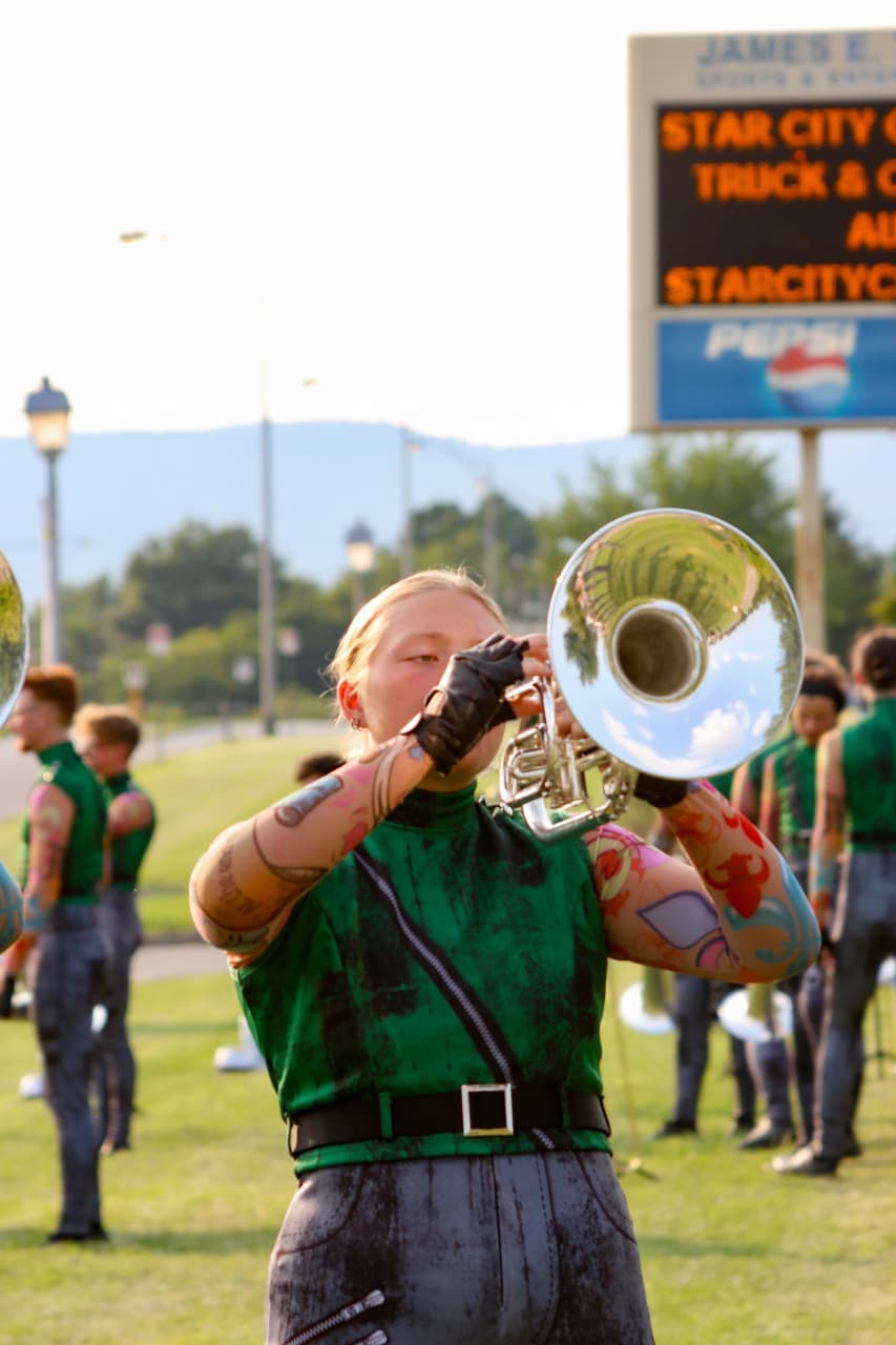 Emma playing mellophone during a lot warm-up with corps members behind her