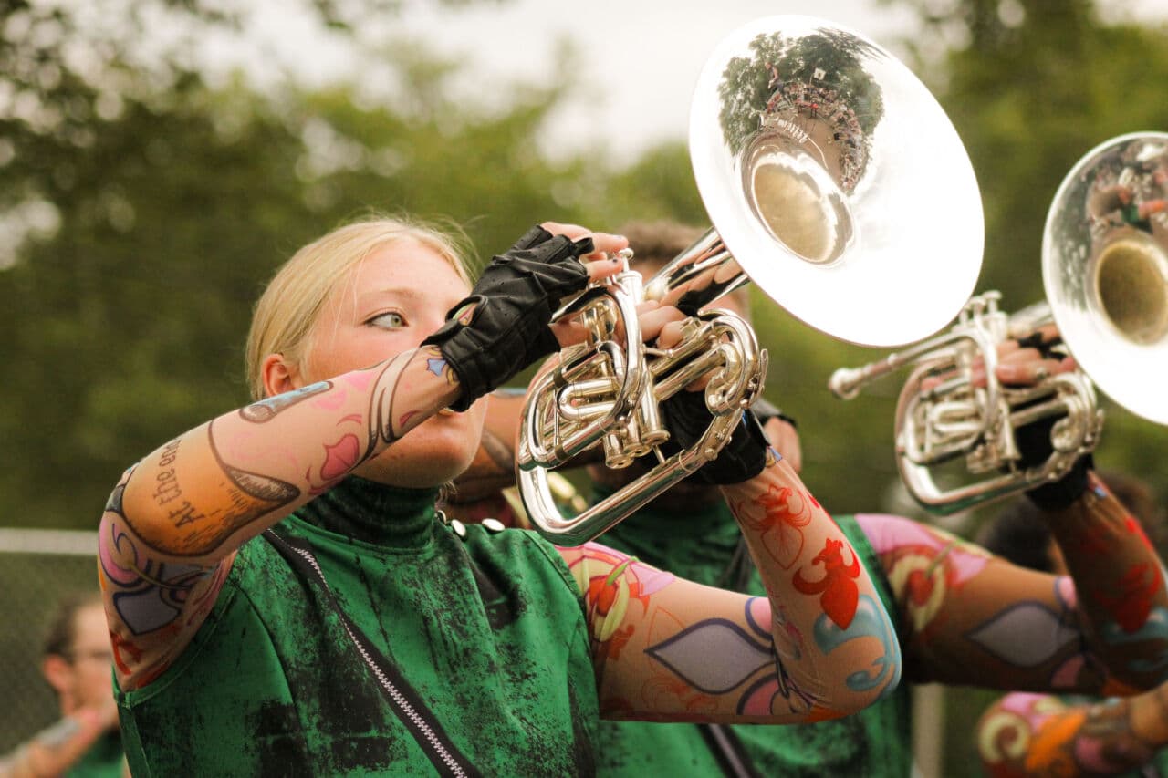 Close-up of Emma playing mellophone in green show costume with colorful body art