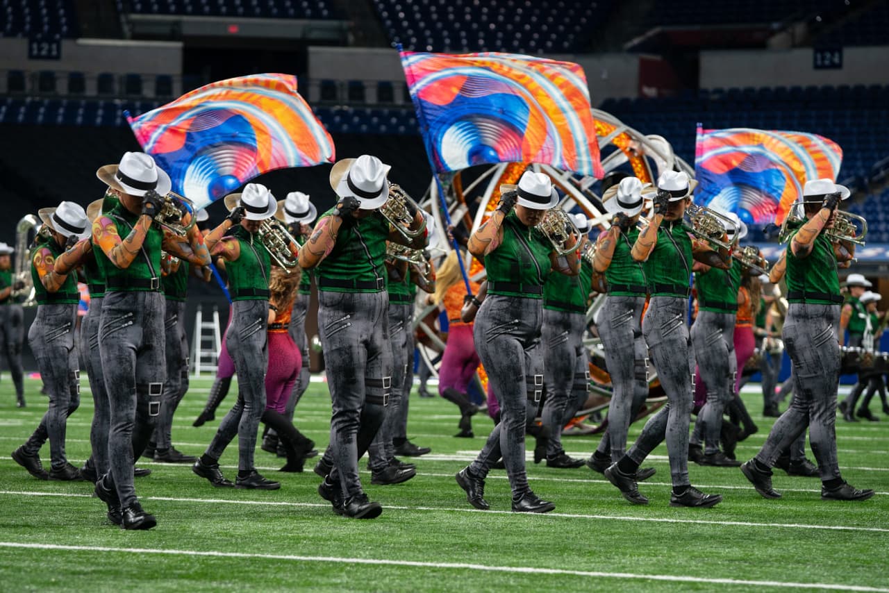 Emma performing mellophone outdoors in full green costume with body art