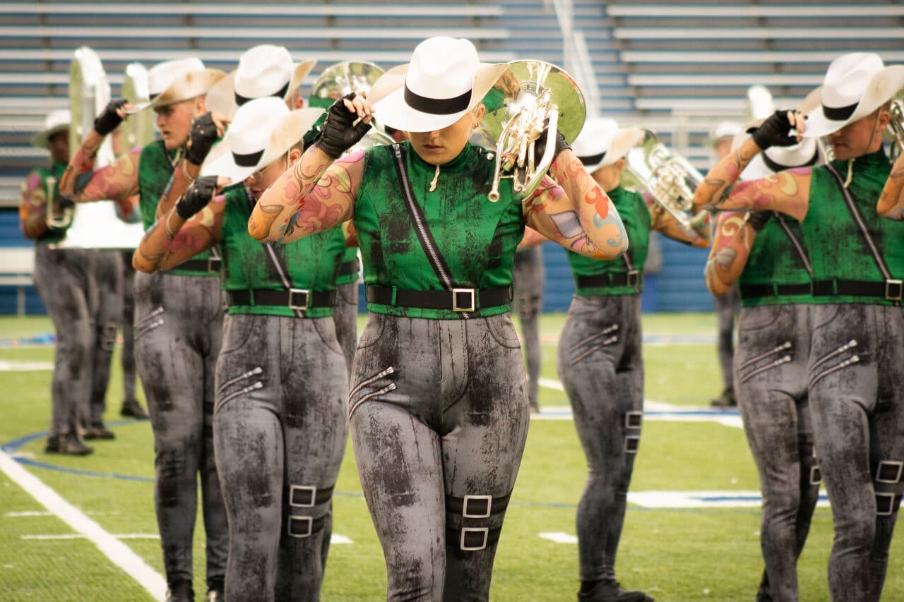Brass line performing in green costumes and white hats on the stadium field
